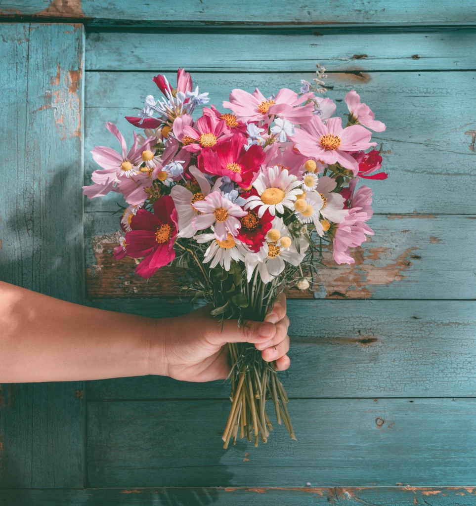 Hand holding bouquet of flowers on background of blue wood.